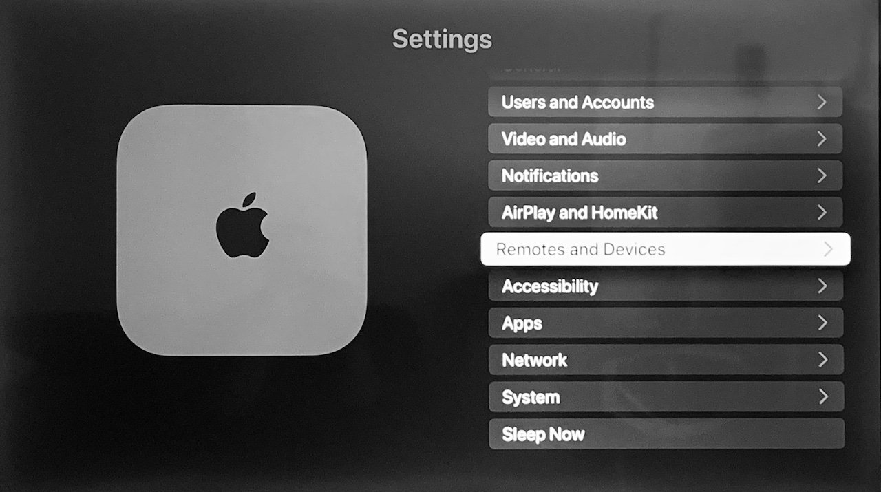 Černobílá fotografie rozhraní Apple TV s různými možnostmi nabídky, jako je Nastavení, Usnadnění a Síť.