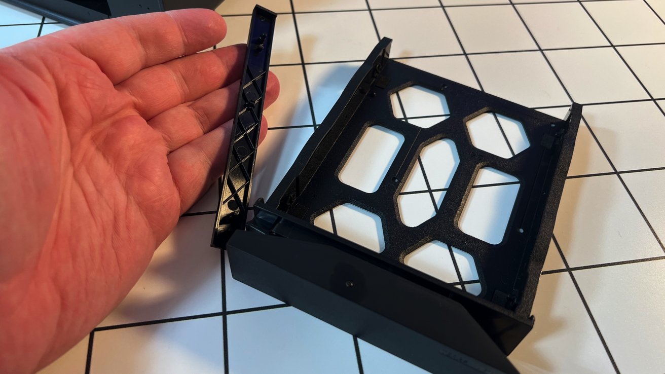 Ruka držící odnímatelný kus z černého plastového pouzdra elektroniky umístěné na bílém dlážděném povrchu.