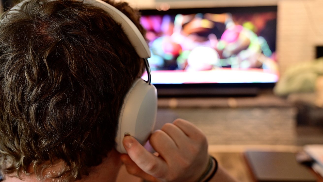 Osoba se sluchátky sleduje barevnou, rozmazanou televizní obrazovku v pozadí.