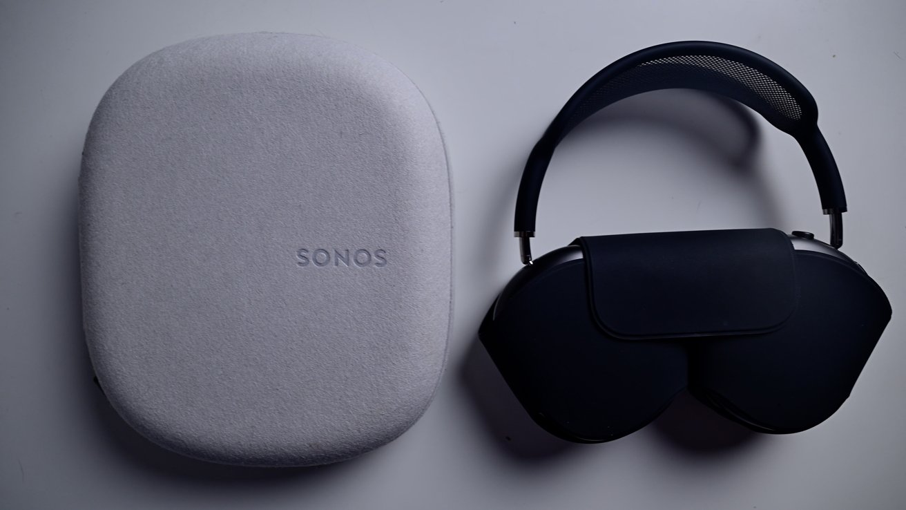 Bílé pouzdro s označením 'SONOS' vedle černých sluchátek přes uši se síťovanou čelenkou na bílém povrchu.